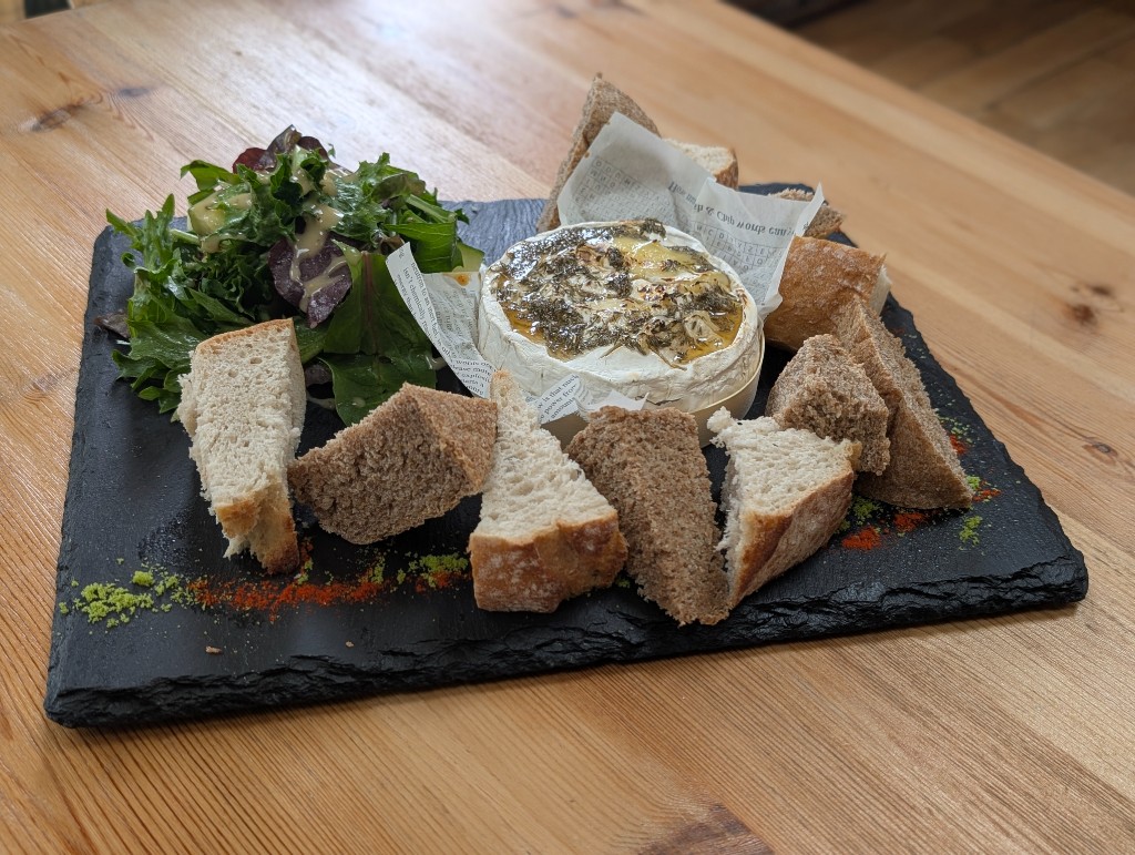 Baked cheese platter with bread and salad on a slate board